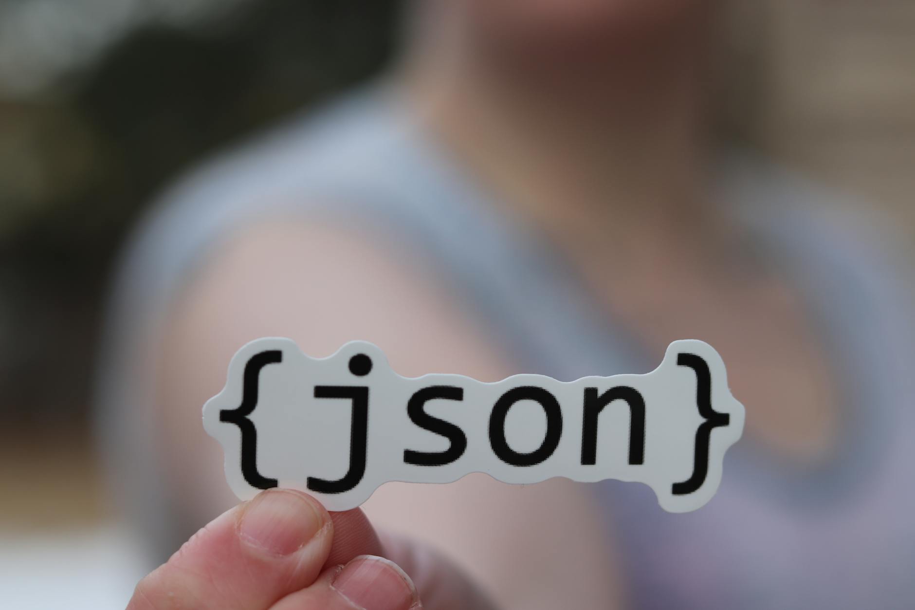 Dłoń trzymająca naklejkę z napisem JSON, symbolizująca tworzenie API
