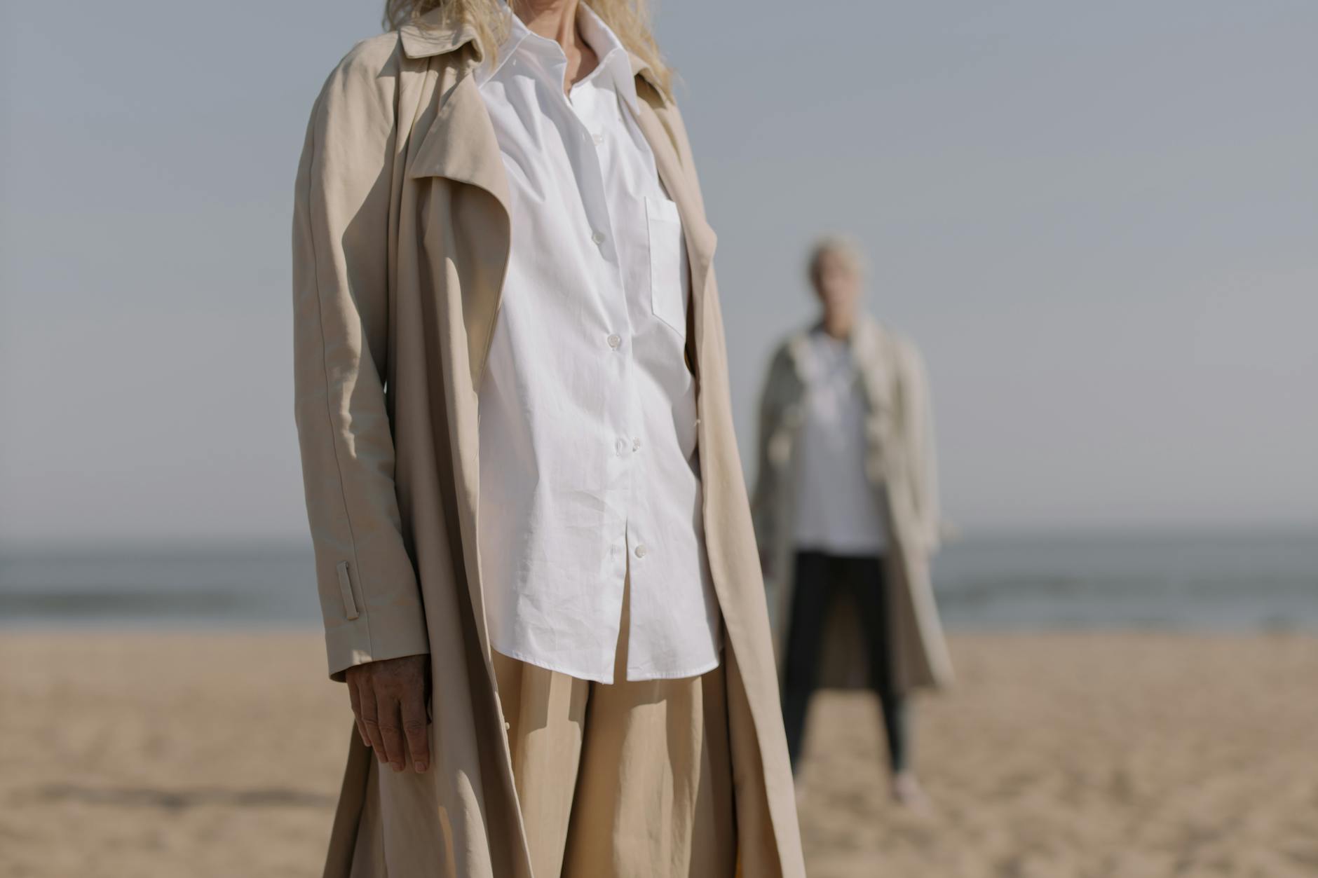 Eleganckie kobiety w beżowych trenczach spacerują po piaszczystej plaży