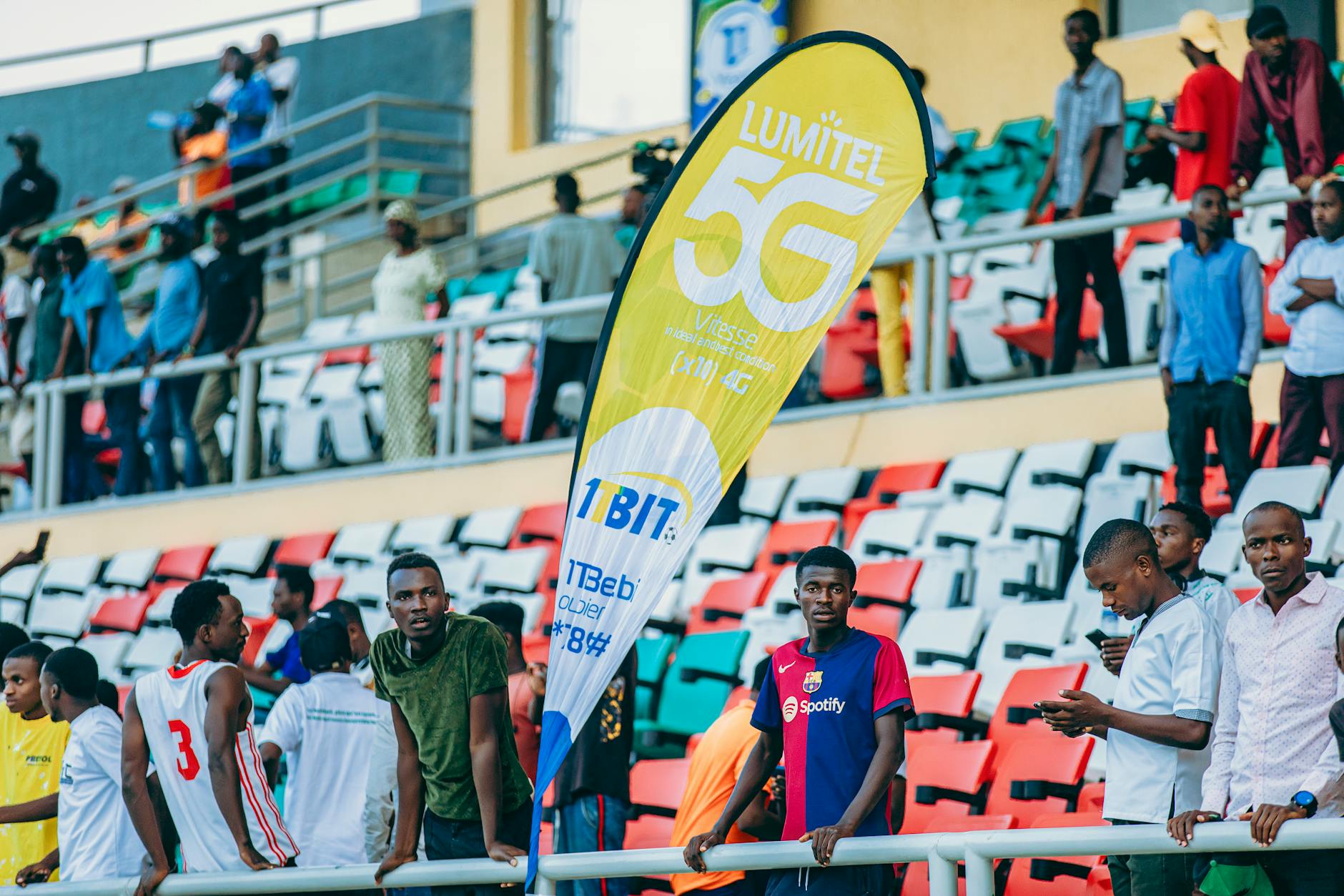 Tłum kibiców na stadionie obok baneru reklamującego sieć Lumitel 5G